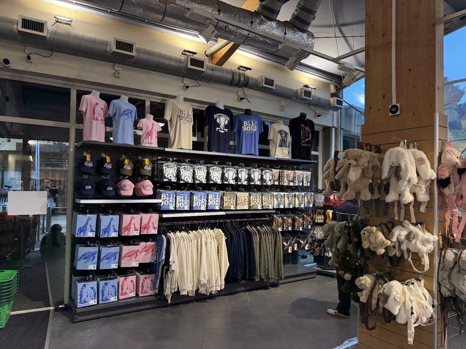 Wandopstelling bij de pui met kleding, petten en knuffelrugzakken